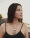 Woman wearing a black tank top with a necklace, standing outdoors.