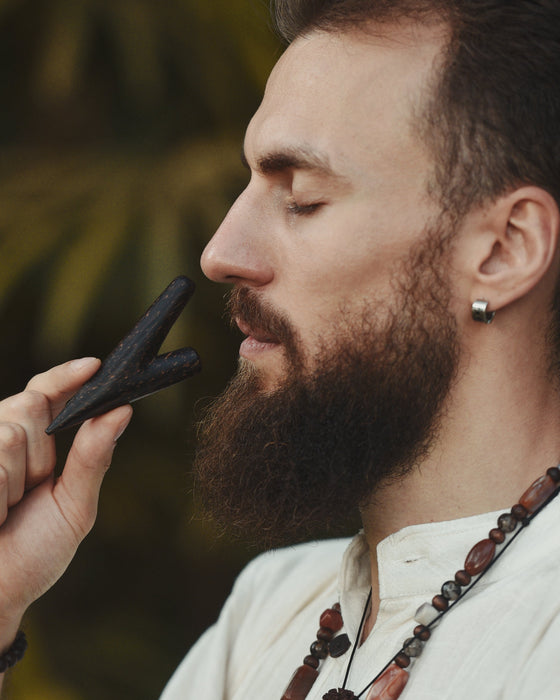 Man with a beard holding a black object close to his face against a blurred natural background