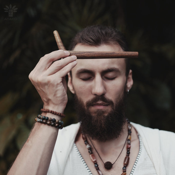 Man with a beard holding two wooden sticks above his eyes with a blurred natural background