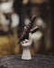 Small ceramic figure of a hand holding two sticks against a blurred natural background