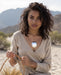 Woman in a beige dress with a necklace, holding a basket, against a desert background