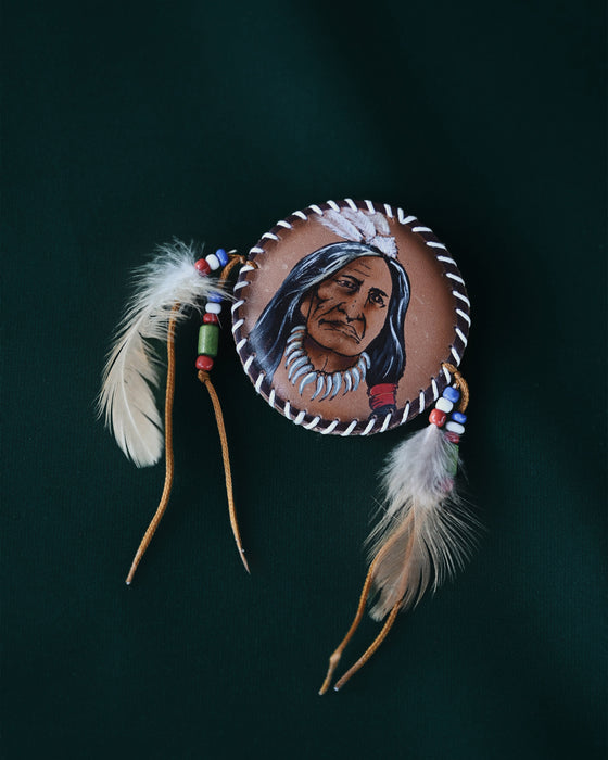 Close-up of a natural pheasant feather brooch with leather wrapping and brass details, pinned to a textured linen jacket.
