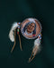 Close-up of a natural pheasant feather brooch with leather wrapping and brass details, pinned to a textured linen jacket.