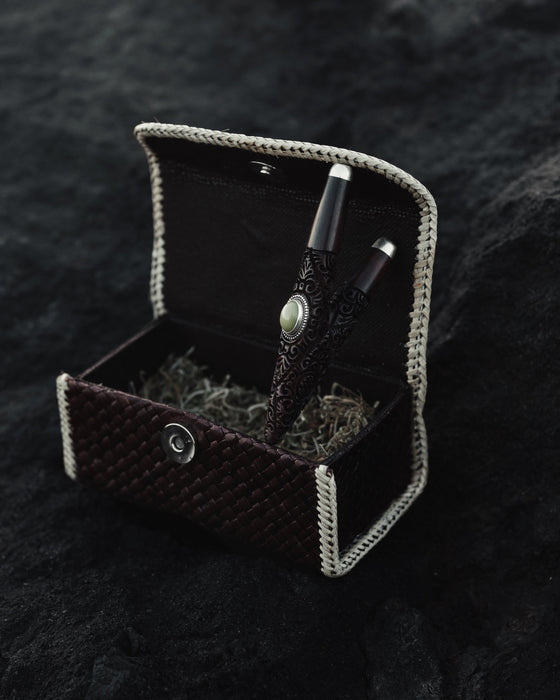 Decorative box with a black pen and silver accents on a textured black surface