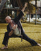 Man in a suit performing a martial arts move outdoors on grass