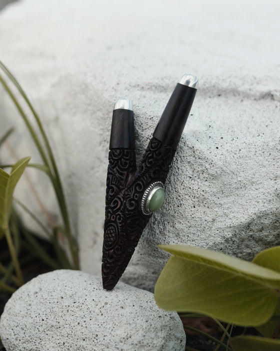 Two black ornate objects with silver tops on a textured surface with green leaves.