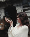 Woman holding a smoking incense bowl in front of a dark, textured wall.