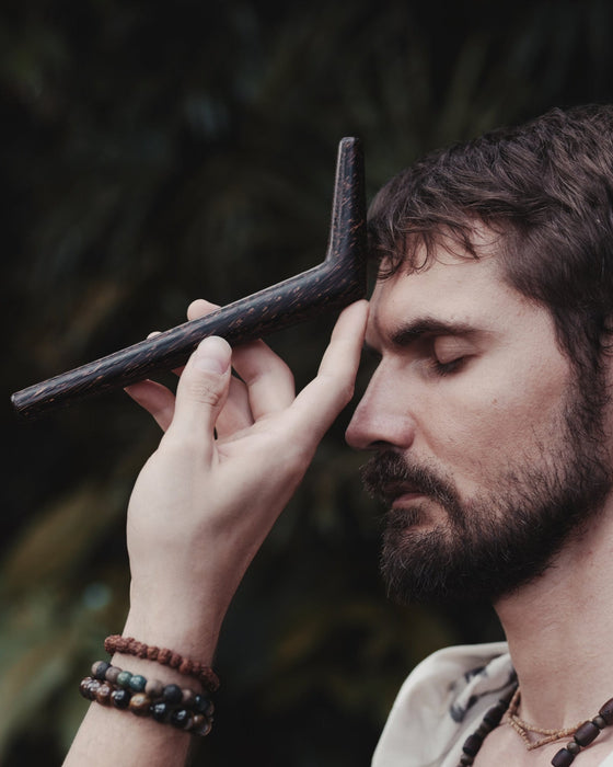 Man holding a long, thin object against his temple with a blurred natural background