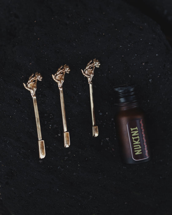 Three gold hair sticks with horse designs and a small bottle labeled 'INLAN' on a dark background.