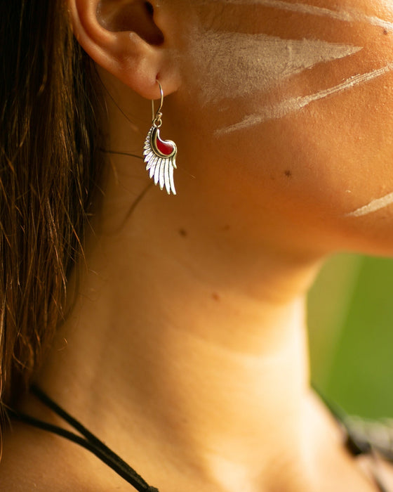 Close-up of a woman's face with white markings on her cheek, wearing a feather earring.