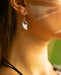 Close-up of a woman's face with white markings on her cheek, wearing a feather earring.