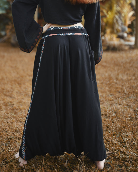 Person wearing a long black skirt with decorative trim in a natural setting