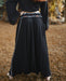 Person wearing a long black skirt with decorative trim in a natural setting