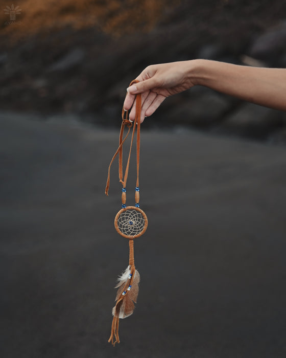 Close-up of a traditional-style dream catcher amulet with amethyst and howlite beadsx, hanging from a car mirror.