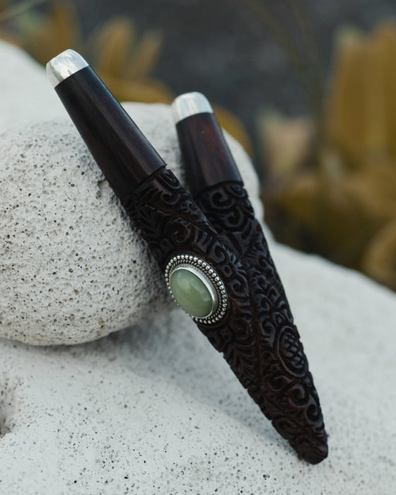 Decorative pen with intricate design and green stone on a textured surface