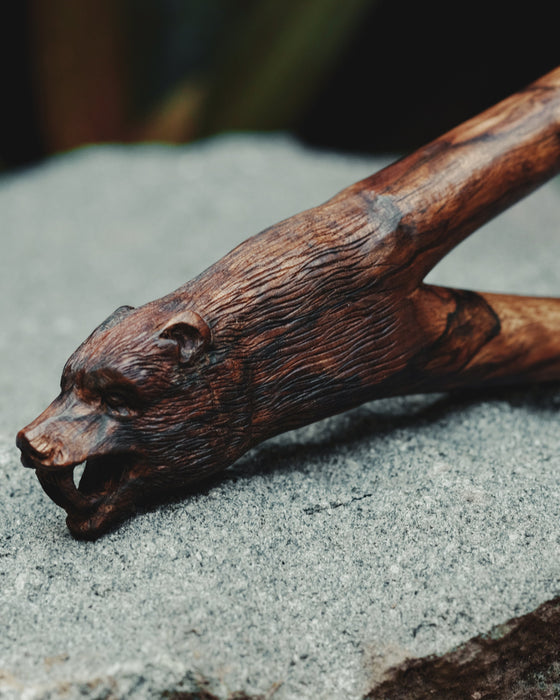 Wooden walking stick with bear head carvings on a stone surface
