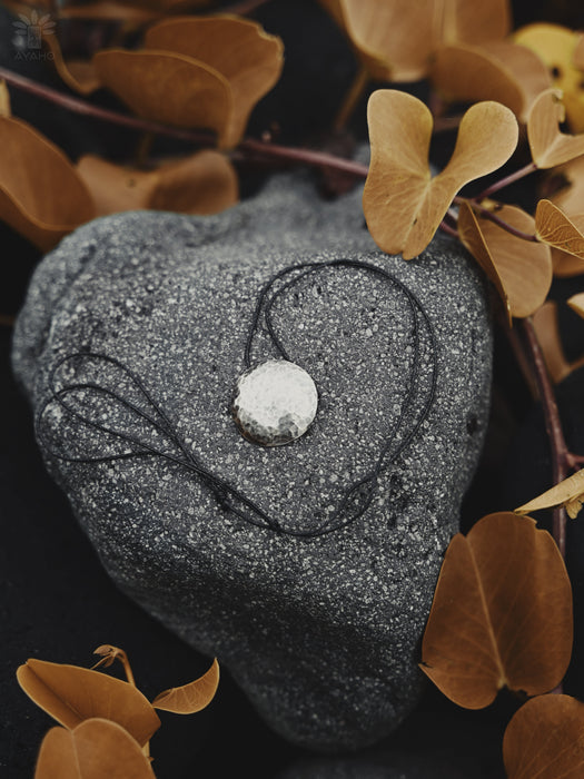 Heart-shaped stone with a necklace on a dark background with brown leaves