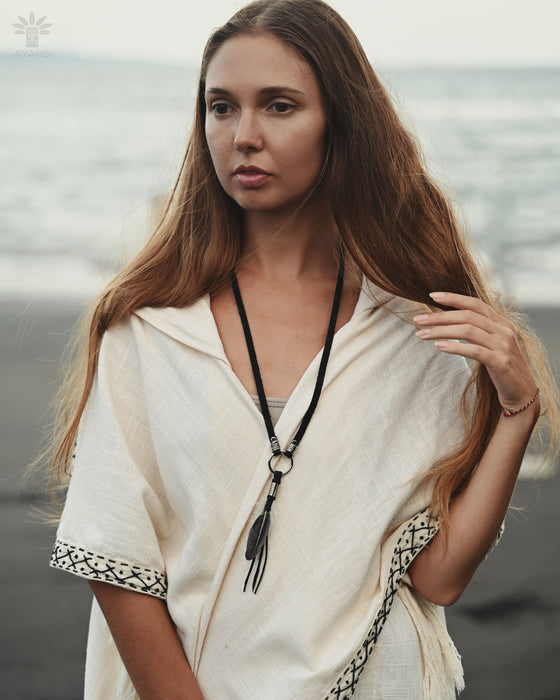 Handmade feather charm with turquoise beads and leather cord, resting on a bed of sage and dried flowers for a natural boho vibe.