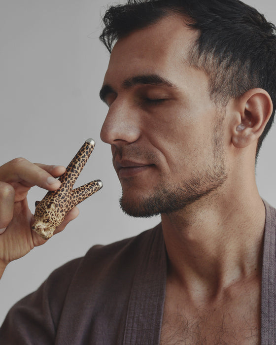 Man holding a leopard-print object near his face against a neutral background