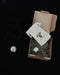 Necklace with pendant, small bag, and decorative stones in a cardboard box on a black background