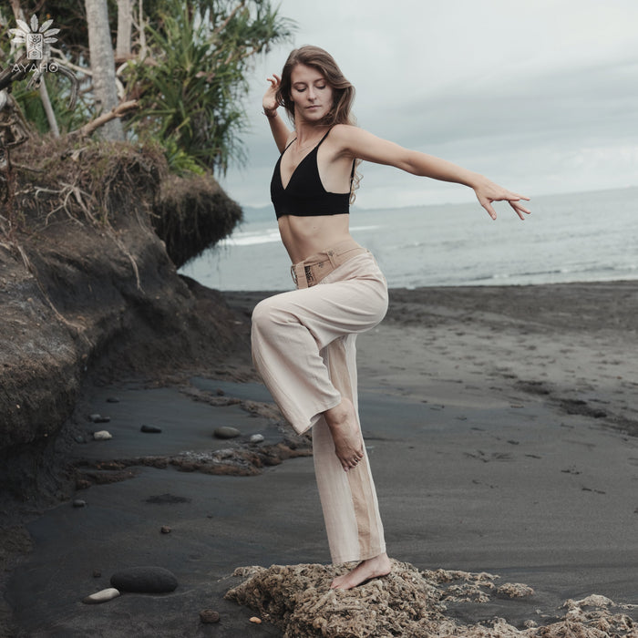 Woman in black top and beige pants standing on a rocky beach with ocean and sky in the background