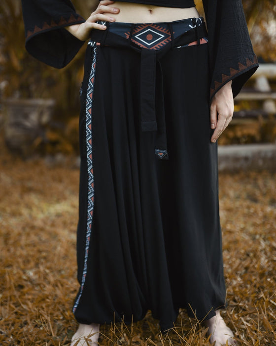 Person wearing a black outfit with patterned trim standing on a natural background
