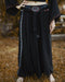 Person wearing a black outfit with patterned trim standing on a natural background