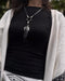 Black raven feather encased in resin with silver wire wrapping, hanging from a black leather choker for an edgy spiritual look