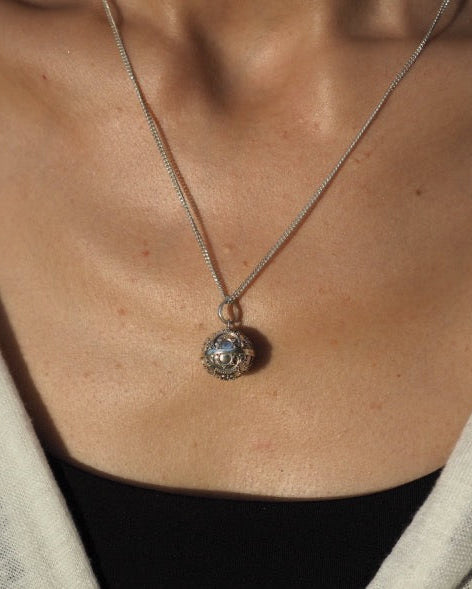 Detailed view of a handcrafted silver harmony bell pendant, serving as a talisman amulet, associated with heart healing and negative energy protection