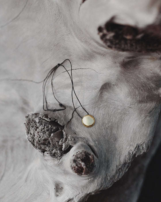 Model wearing a copper shaman mirror necklace, reflecting light onto a flowy linen dress for earthy elegance.