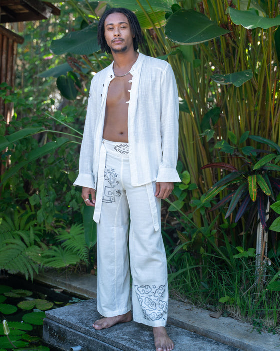 Man in a white outfit standing in a lush green outdoor setting