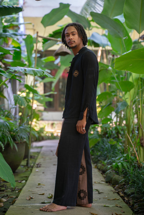 Man in black traditional outfit standing in a lush green garden