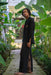 Man in black traditional outfit standing in a lush green garden