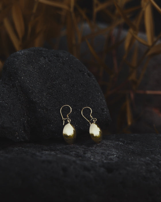 Hand-forged bronze earrings with tiny mirrors, displayed on an altar with feathers and herbs.