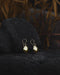 Hand-forged bronze earrings with tiny mirrors, displayed on an altar with feathers and herbs.