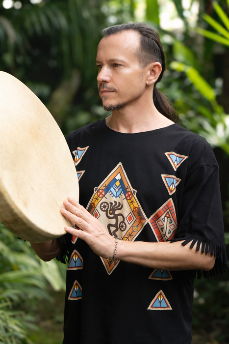 Man holding a drum outdoors with greenery in the background
