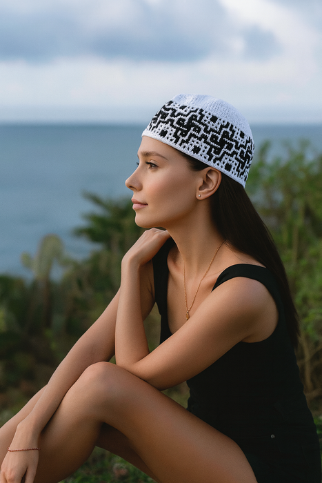 Woman sitting by the ocean wearing a black and white patterned headscarf