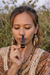 Woman holding a small object close to her face outdoors with a blurred natural background