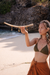 Woman holding a curved object on a beach with rocky cliffs in the background
