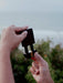 Person holding a small black device with a blurred natural background