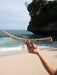Hand holding a piece of driftwood with gold jewelry against a beach backdrop