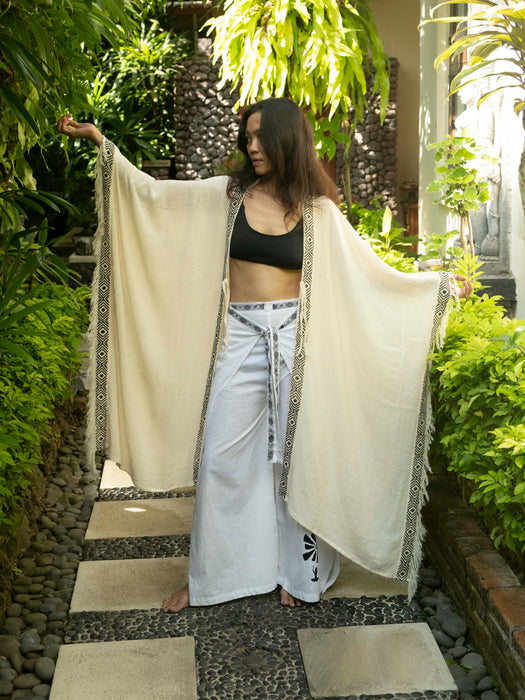 Woman holding a long, light-colored garment in an outdoor setting with greenery.