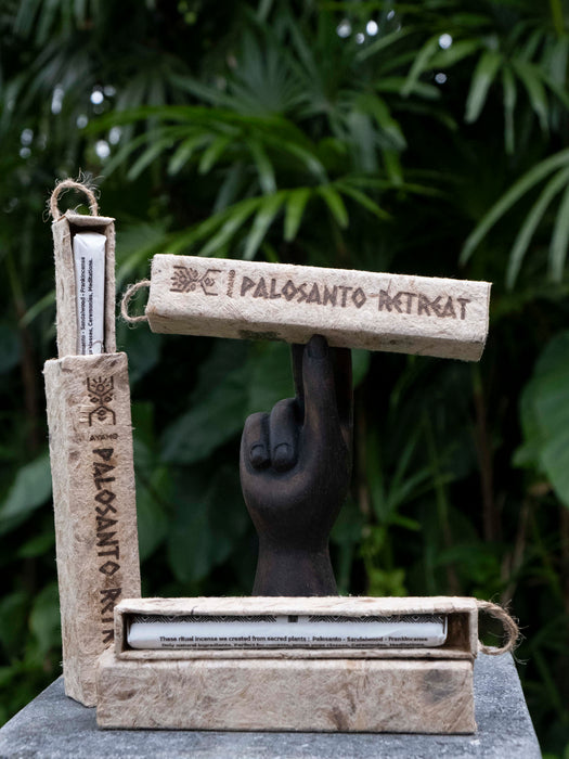 Three wooden incense holders with 'Palosanto Retreat' branding against a green leafy background.
