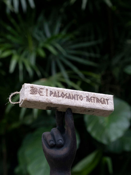 Palosanto retrogat incense stick held by a statue hand with green foliage in the background