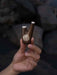 Hand holding a wooden tool with intricate carvings against a blurred natural background