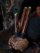 Wooden mace with metal handles on a wooden stand, surrounded by peacock feathers and other items.