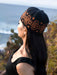 Woman wearing a black knit beanie with orange patterns, standing outdoors near water.