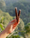 Hand holding two wooden slingshots with intricate designs against a blurred natural background