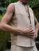 Man wearing a beige sleeveless vest over a shirt with a blurred natural background