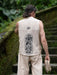 Person wearing a sleeveless beige shirt with a black design, standing outdoors.